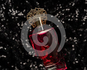 Glass bottle with pink perfume liquid on black background with shiny sequins