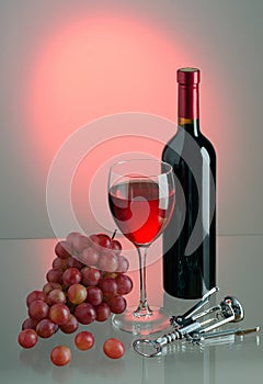 Glass and bottle with red wine, grapes and corkscrew on colored background