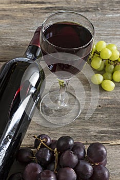 Glass and bottle of red wine and grapes on a old wooden background