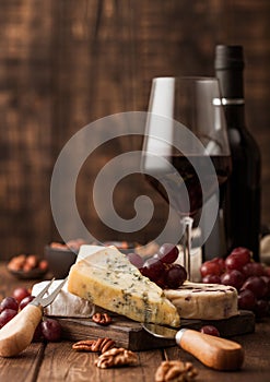 Glass and bottle of red wine with selection of various cheese on the board and grapes on wooden background. Blue Stilton, Red