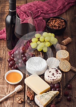 Glass and bottle of red wine with selection of various cheese on the board and grapes on wooden background. Blue Stilton, Red