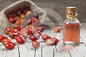 Glass bottle of rosehip seed essential oil with fresh rose hip fruits on wooden rustic background photo