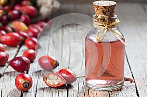 Glass bottle of rosehip seed essential oil with fresh rose hip fruits on wooden rustic background photo