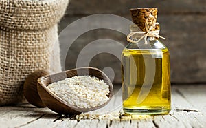 Glass bottle of sesame oil and raw sesame seeds in wooden shovel or spoon on burlap sack