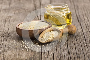 Glass bottle of sesame oil and raw sesame seeds in wooden shovel with burlap sack on wooden table