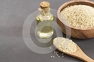 Glass bottle of sesame oil and raw sesame seeds in wooden shovel with burlap sack on wooden table