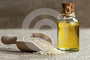 Glass bottle of sesame oil and raw sesame seeds in wooden shovel or spoon on burlap sack