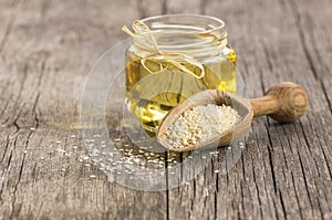 Glass bottle of sesame oil and raw sesame seeds in wooden shovel on wooden table