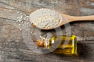 Glass bottle of sesame oil and raw sesame seeds in wooden spoon on wooden table