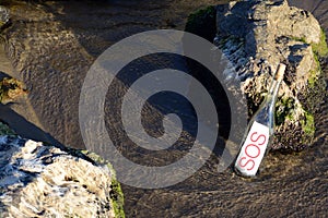 Glass bottle with SOS message near sea rocks, space for text