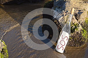 Glass bottle with SOS message near sea rocks, space for text