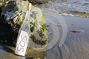 Glass bottle with SOS message near sea rocks, space for text