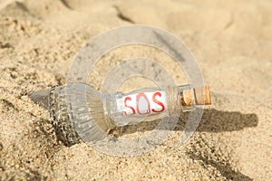 Glass bottle with SOS message on sand, closeup