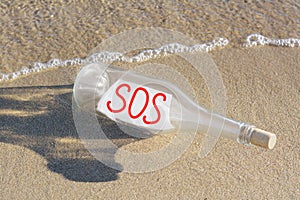 Glass bottle with SOS message on sand near sea