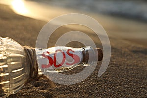 Glass bottle with SOS message on sand near sea, closeup