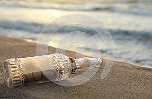 Glass bottle with SOS message on sand near sea, closeup