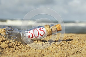 Glass bottle with SOS message on sand near sea, closeup