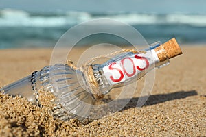 Glass bottle with SOS message on sand near sea, closeup