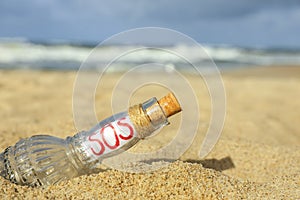 Glass bottle with SOS message on sand near sea, closeup