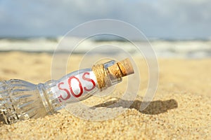 Glass bottle with SOS message on sand near sea, closeup