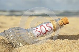 Glass bottle with SOS message on sand near sea, closeup