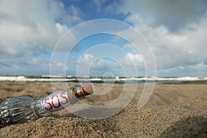 Glass bottle with SOS message on sand near sea, space for text