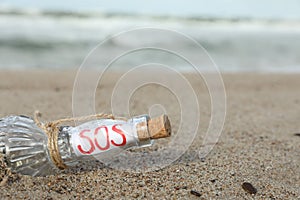 Glass bottle with SOS message on sand near sea, space for text