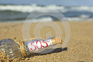 Glass bottle with SOS message on sand near sea, space for text