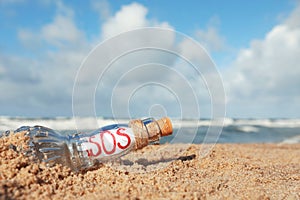 Glass bottle with SOS message on sand near sea, space for text