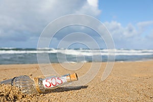 Glass bottle with SOS message on sand near sea, space for text