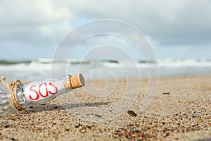 Glass bottle with SOS message on sand near sea, space for text