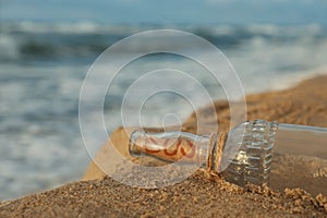 Glass bottle with SOS message on sand near sea, space for text