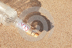 Glass bottle with SOS message on sand, top view