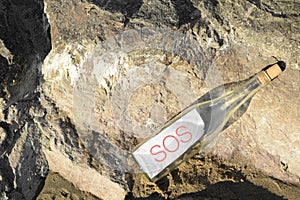 Glass bottle with SOS message on sea rock, top view