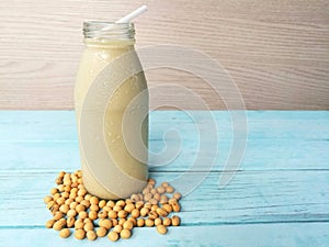 A glass bottle soy milk, soybeans seed around base, blue wooden table,