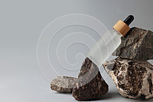 Glass bottle and stones on grey background, space for text