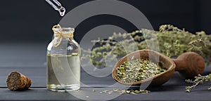 Glass bottle of thyme essential oil and bunch of dry thyme on black wooden rustic background