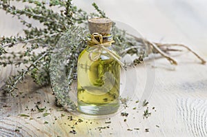 Glass bottle of thyme essential oil and bunch of dry thyme on wooden rustic background