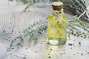 Glass bottle of thyme essential oil and bunch of dry thyme on wooden rustic background