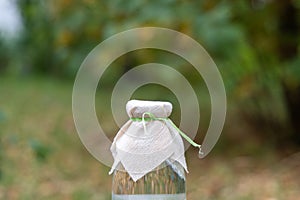 A glass bottle with a transparent drink or water with a lid made of natural linen fabric stands on an outdoor stone in