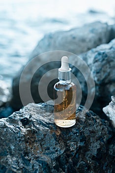 Glass bottle with vitamin serum on the rocks on a sea shore
