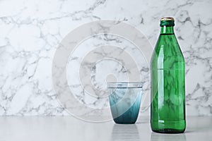 Glass and bottle with water on table against white marble background, space for text