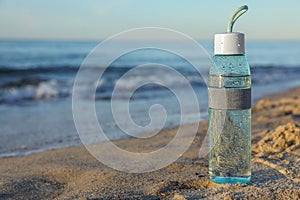 Glass bottle with water on wet sand near sea. Space for text