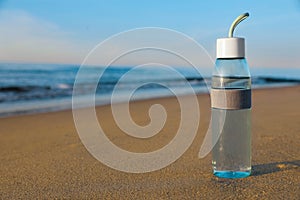 Glass bottle with water on wet sand near sea. Space for text