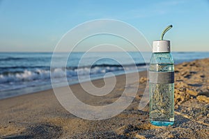 Glass bottle with water on wet sand near sea. Space for text