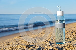 Glass bottle with water on wet sand near sea. Space for text