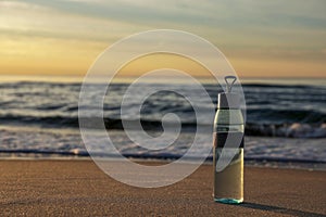 Glass bottle with water on wet sand near sea at sunset. Space for text