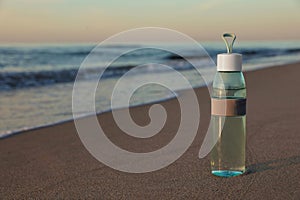 Glass bottle with water on wet sand near sea at sunset. Space for text