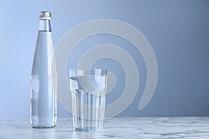 Glass and bottle with water on white marble table against blue background, space for text
