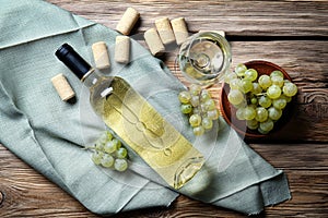 Glass and bottle of white wine with fresh grapes on wooden table